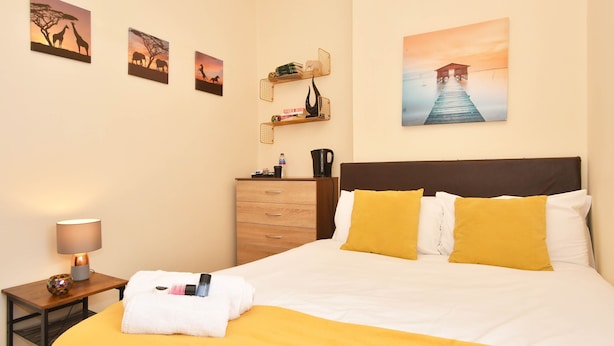 A hotel room with a bed, a nightstand with a lamp, a dresser, and wall art. - Townhouse @ 178 Ruskin Road Crewe (Crewe)