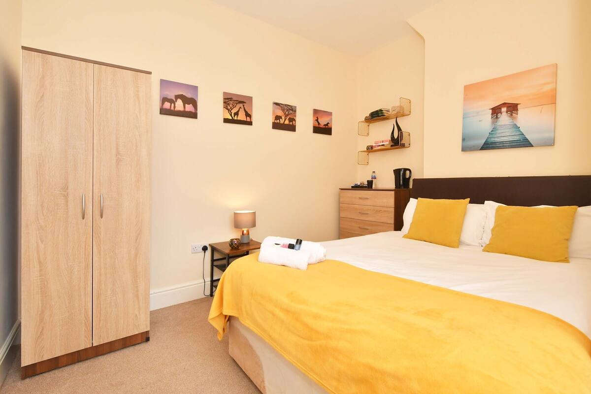 A bedroom with a bed, a wardrobe, a nightstand with a lamp, and wall art.