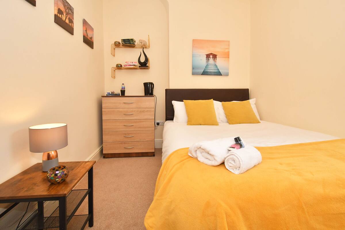 A neatly arranged hotel room with a bed, a nightstand, a dresser, and a wall with artwork.