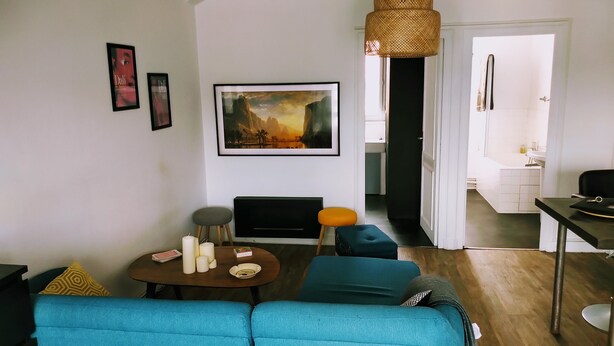 A living room with a sofa, a small table with candles, a painting, and a doorway leading to a bathroom. - Connected studio with open view - CENTRE-VILLE (Nantes)