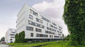 A modern multi-story building with a flat roof, large windows, and a landscaped garden area with neatly trimmed hedges. - Stylish Apartment with a Balcony | Parking | Close to Kazimierz (Kraków)