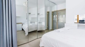 A modern hotel room with a large bed, a glass partition wall, and a small seating area with a chair and table. - Stylish Apartment with a Balcony | Parking | Close to Kazimierz (Kraków)
