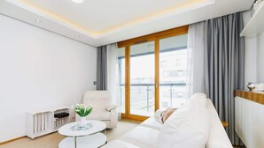 A modern living room with a white sofa, a round coffee table, and a view of the outside through large windows. - Stylish Apartment with a Balcony | Parking | Close to Kazimierz (Kraków)