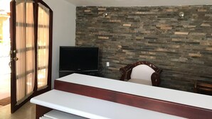 Una habitación con pared de piedra, televisor, silla de madera y mostrador blanco.