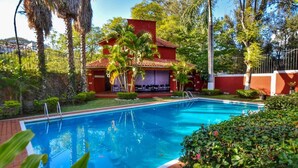 Una piscina con un edificio rojo al fondo, rodeada de vegetación.