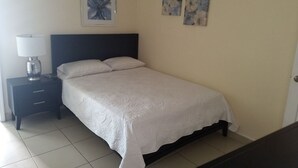 A neatly made bed with a white bedspread, a dark headboard, and a nightstand with a lamp and a small decorative item. - Beautiful House on 2nd Floor (Close to the airport!)  (Tijuana)