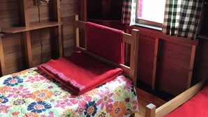 A cozy room with a wooden bed, a small table with a lamp, and a window with checkered curtains. - Airy Wooden Beach House with Big Private Deck, close to Atlantic Ocean Beach or gentler bay swimming.  (Fire Island)