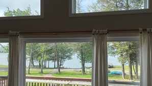A room with a large window overlooking a deck with a wooden railing and picnic tables. - Lovely Mount Storm Waterfront Lake House - pet friendly, child friendly retreat (Mt Storm)