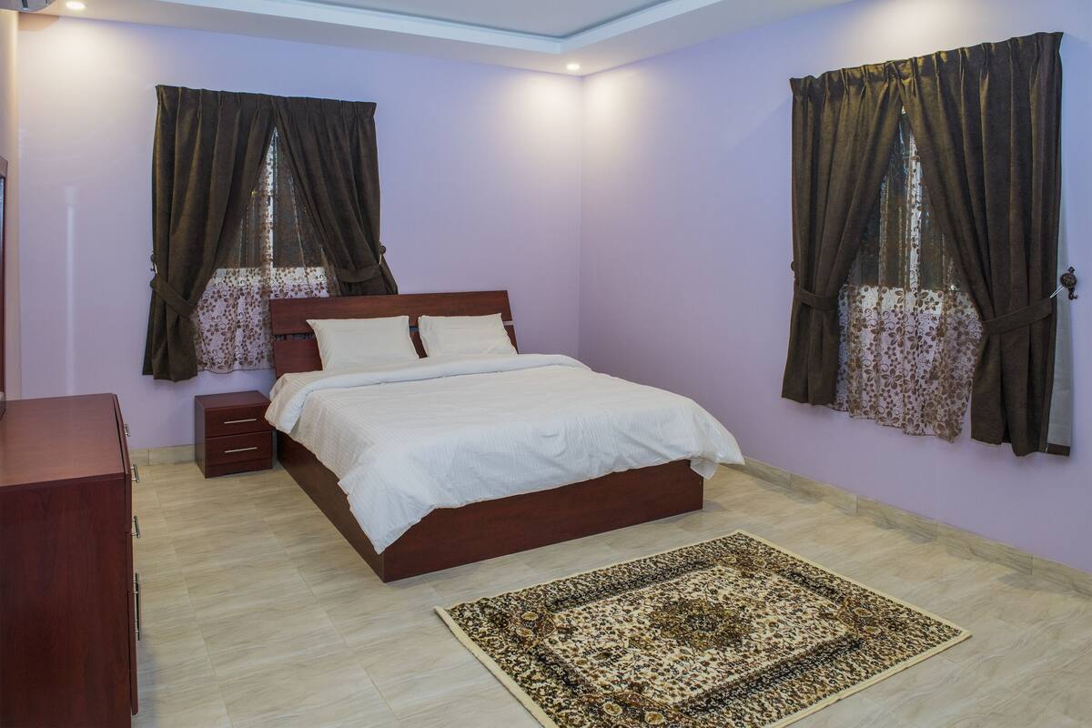 Un dormitorio con una cama de madera, una mesita de noche, un aparador y una alfombra estampada.