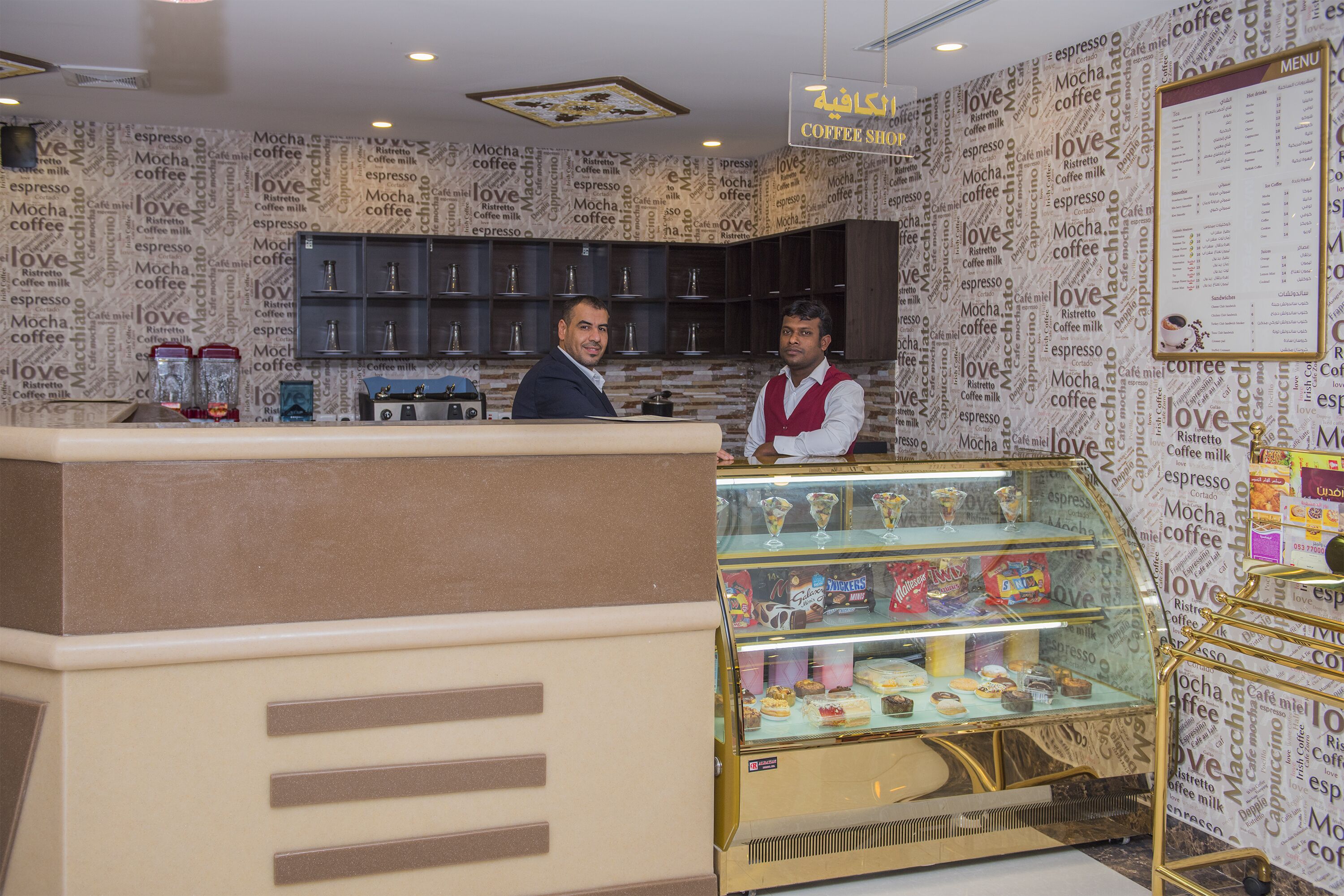 A coffee shop interior with a counter, a display case of pastries, and a menu board.