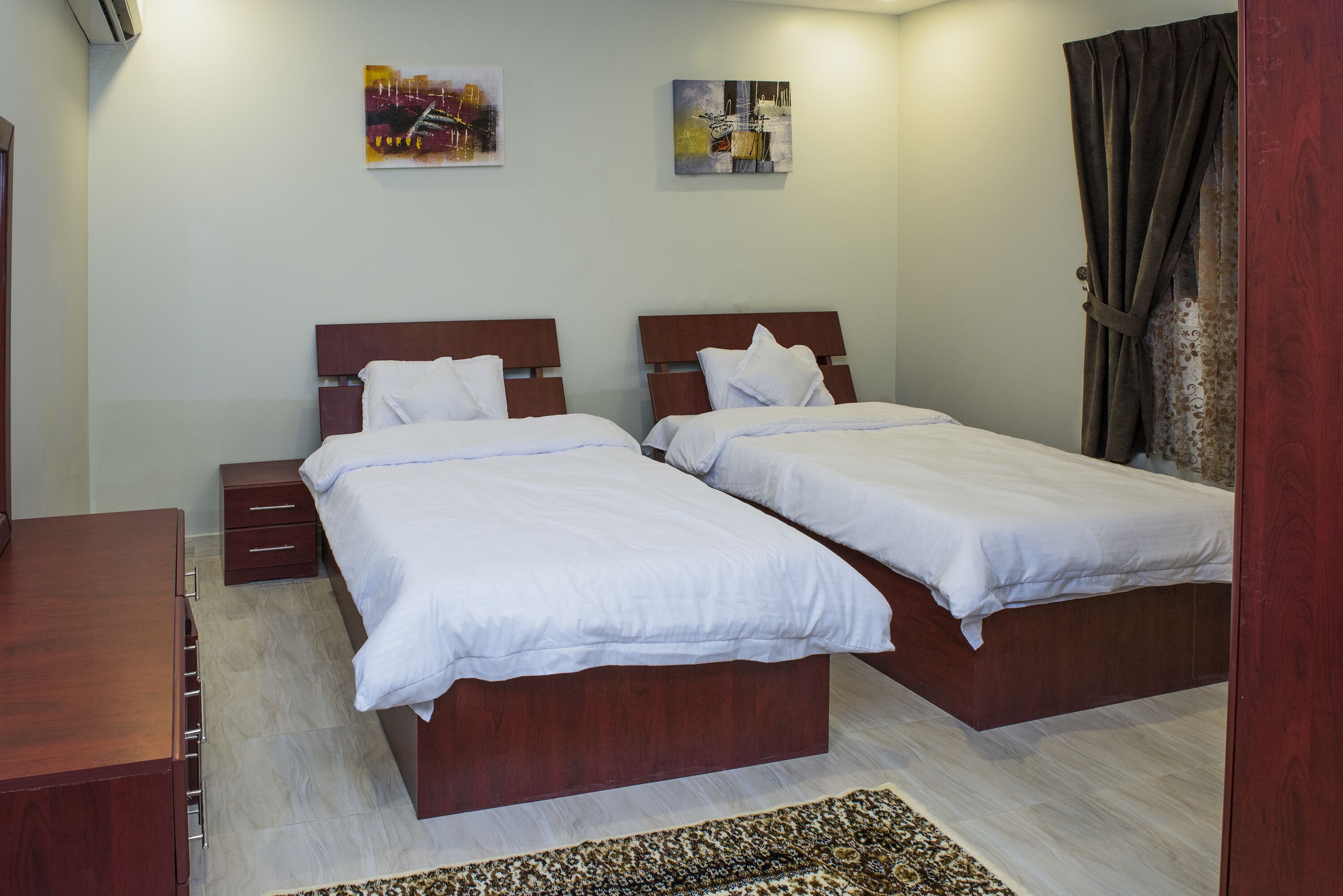 A bedroom with two beds, a wooden dresser, and a patterned rug.