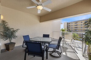 Ein Balkon mit Tisch und Stühlen, Deckenventilator, Topfpflanzen und Blick auf ein Gebäude.
