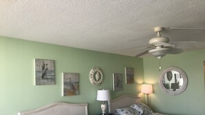 Una habitación con dos camas, ventilador de techo y obras de arte en las paredes.