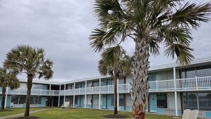Un motel con una estructura de dos pisos, una zona de estacionamiento techada y un césped con palmeras.