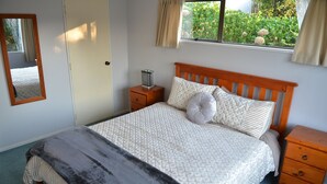 A bedroom with a bed, a nightstand, a mirror, and a window with curtains. - Waitomo Big Bird Retreat (Waitomo)