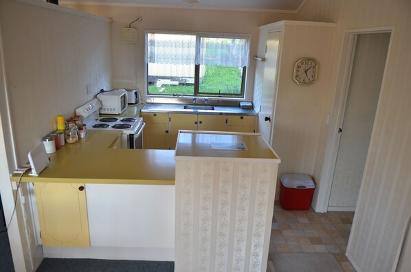 Une cuisine de taille réduite avec un plan de travail jaune, des placards blancs, une cuisinière, un four à micro-ondes et une fenêtre donnant sur l’extérieur.