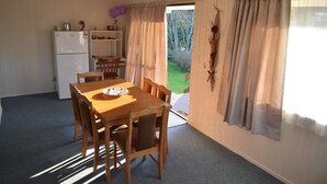 A dining area with a wooden table and chairs, a refrigerator, and a view of a garden through a door. - Waitomo Big Bird Retreat (Waitomo)