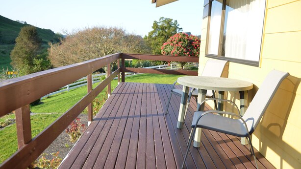 A wooden deck with a table and chairs, overlooking a green landscape with trees and a hill. - Waitomo Big Bird Retreat (Waitomo)