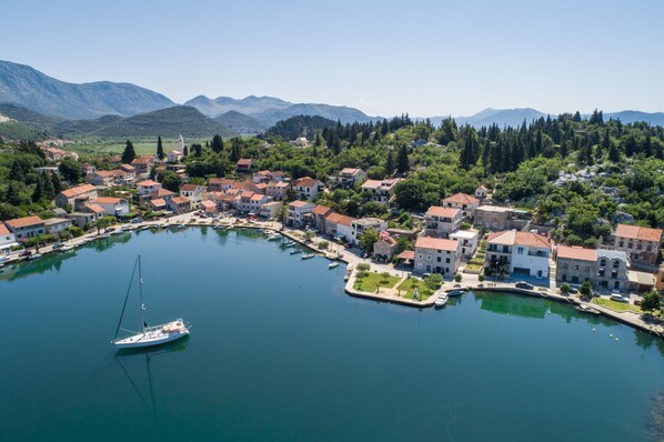 Ein Küstdorf mit Gebäuden entlang des Ufers, ein kleines Boot an einem Anleger und Berge im Hintergrund.