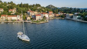A coastal town with buildings along the waterfront, a sailboat docked at the pier, and a hilly backdrop. - Apartments Ema-Comfort Two Bedroom Apartment with Sea View (Rogotin)