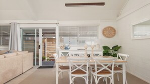 A modern living room with a sofa, a dining table with chairs, and a sliding glass door leading to a balcony. - Little Kingsley Beach House - Back Flat - across the road from the Beach (Boat Harbour)