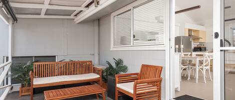 A balcony with wooden furniture, a sliding glass door leading to a kitchen, and a view of the building's interior.