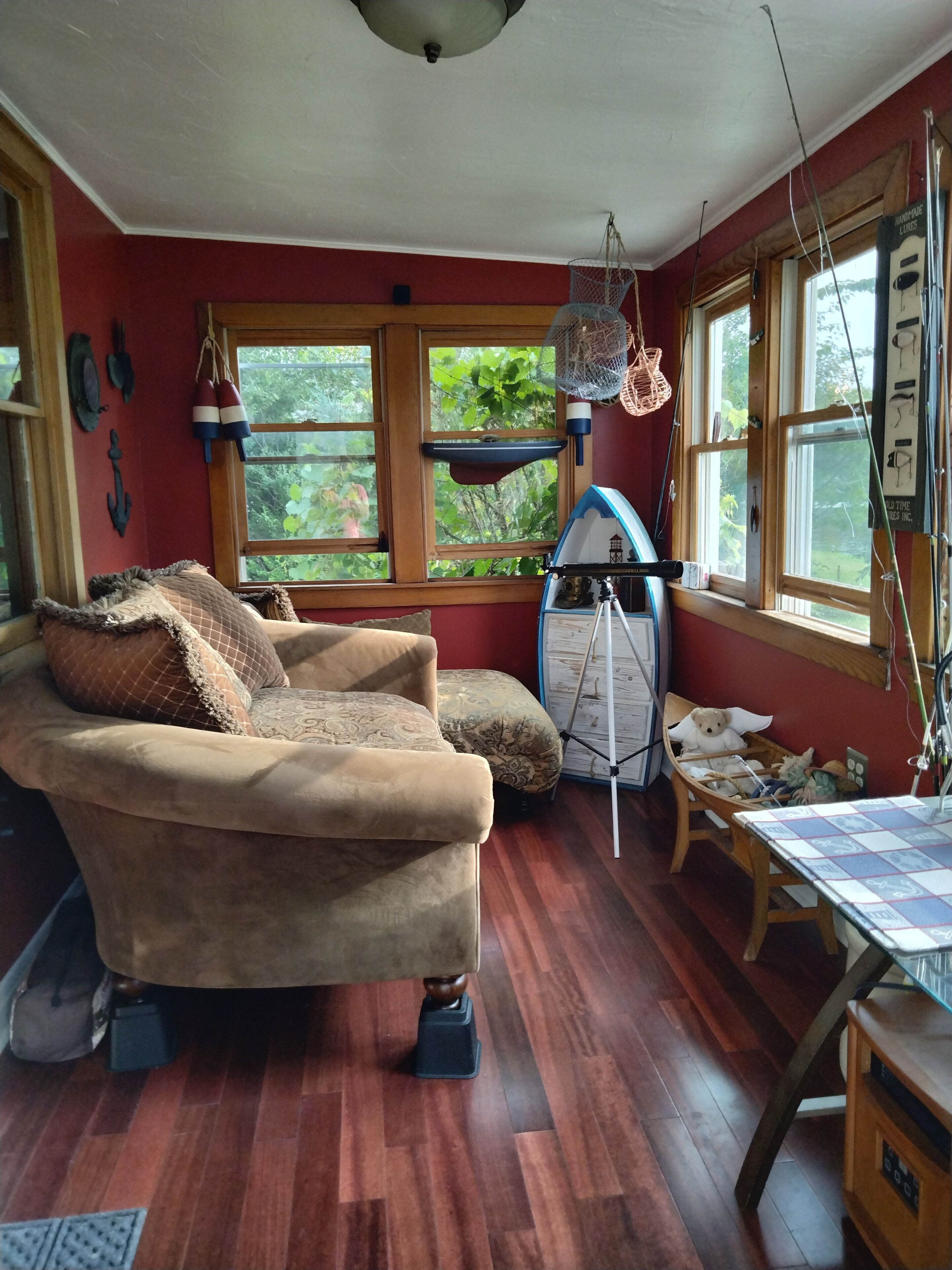 Une pièce chaleureuse avec un canapé vintage, une petite table et un fauteuil à bascule. De grandes fenêtres offrent une vue sur la verdure environnante.
