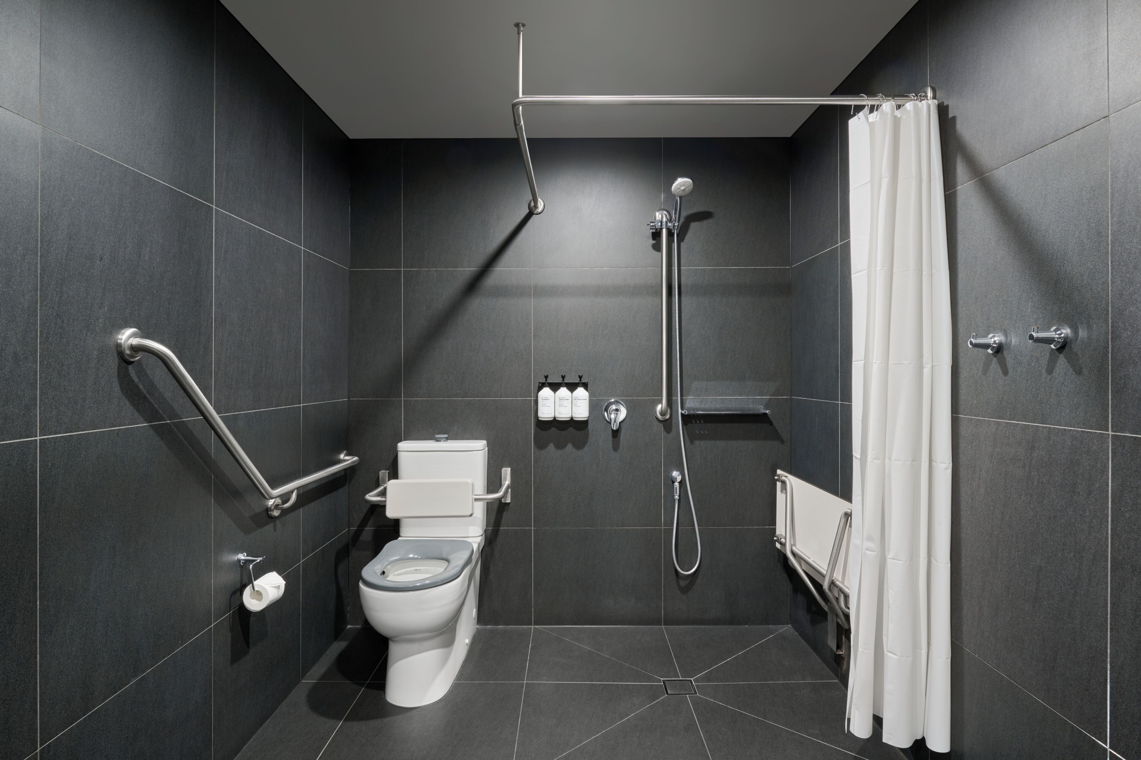 A modern bathroom with a toilet, shower, and grab bars.