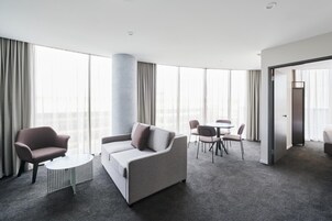 Una habitación de hotel moderna con un sofá gris, una mesa redonda y un comedor con sillas y una mesa.