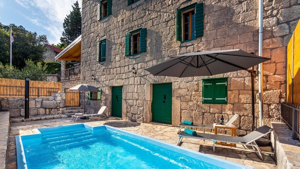 Ein Steinhaus mit Swimmingpool, grünen Fensterläden und Außenbereich mit Sitzmöglichkeiten.