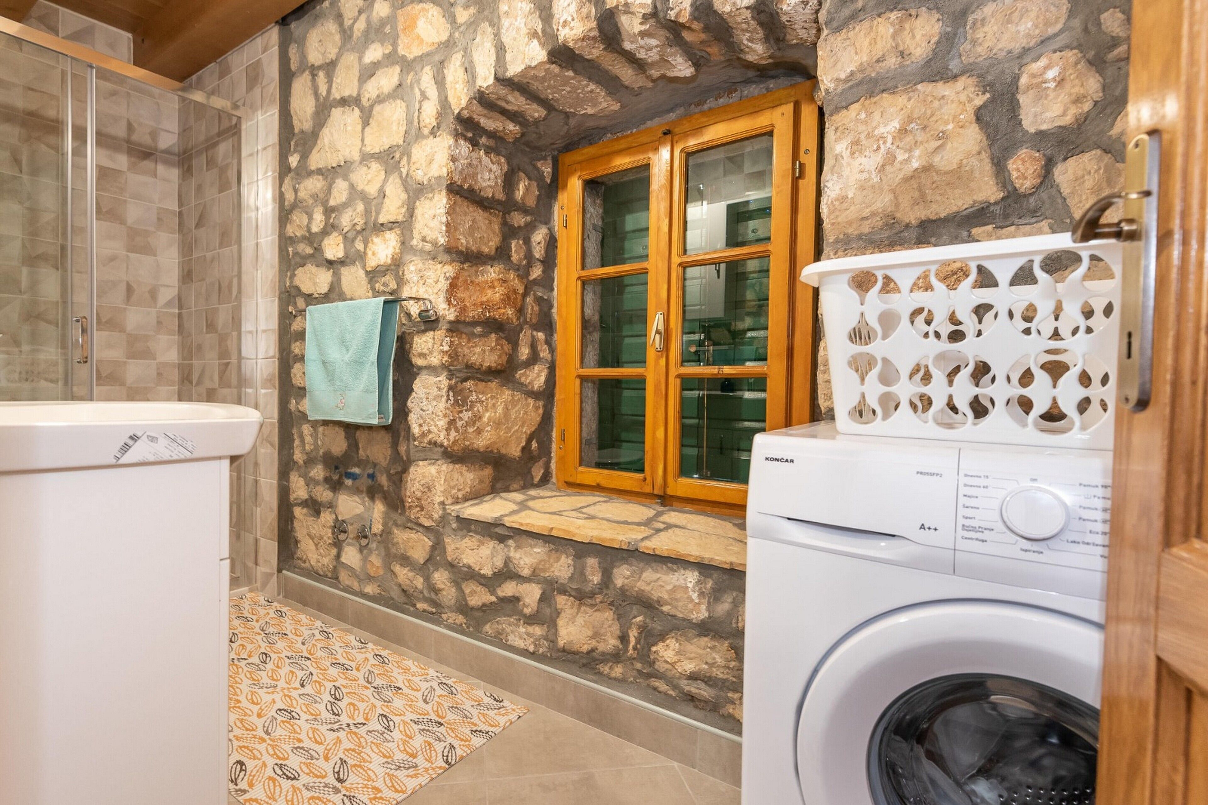 Zona de lavandería con lavadora, ventana con contraventanas de madera y pared de piedra.