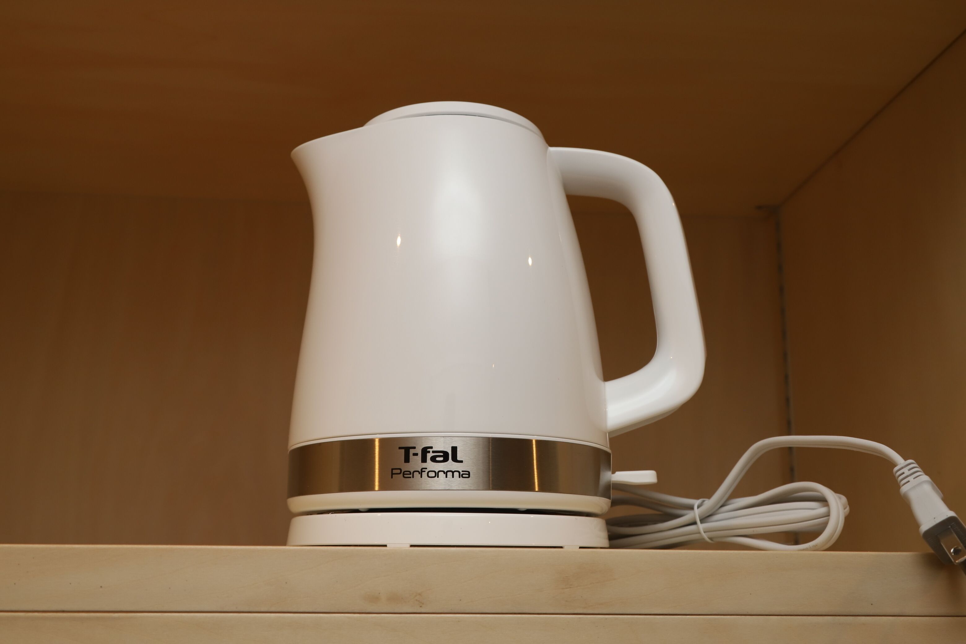 A white electric kettle with a handle and a power cord on a wooden surface.