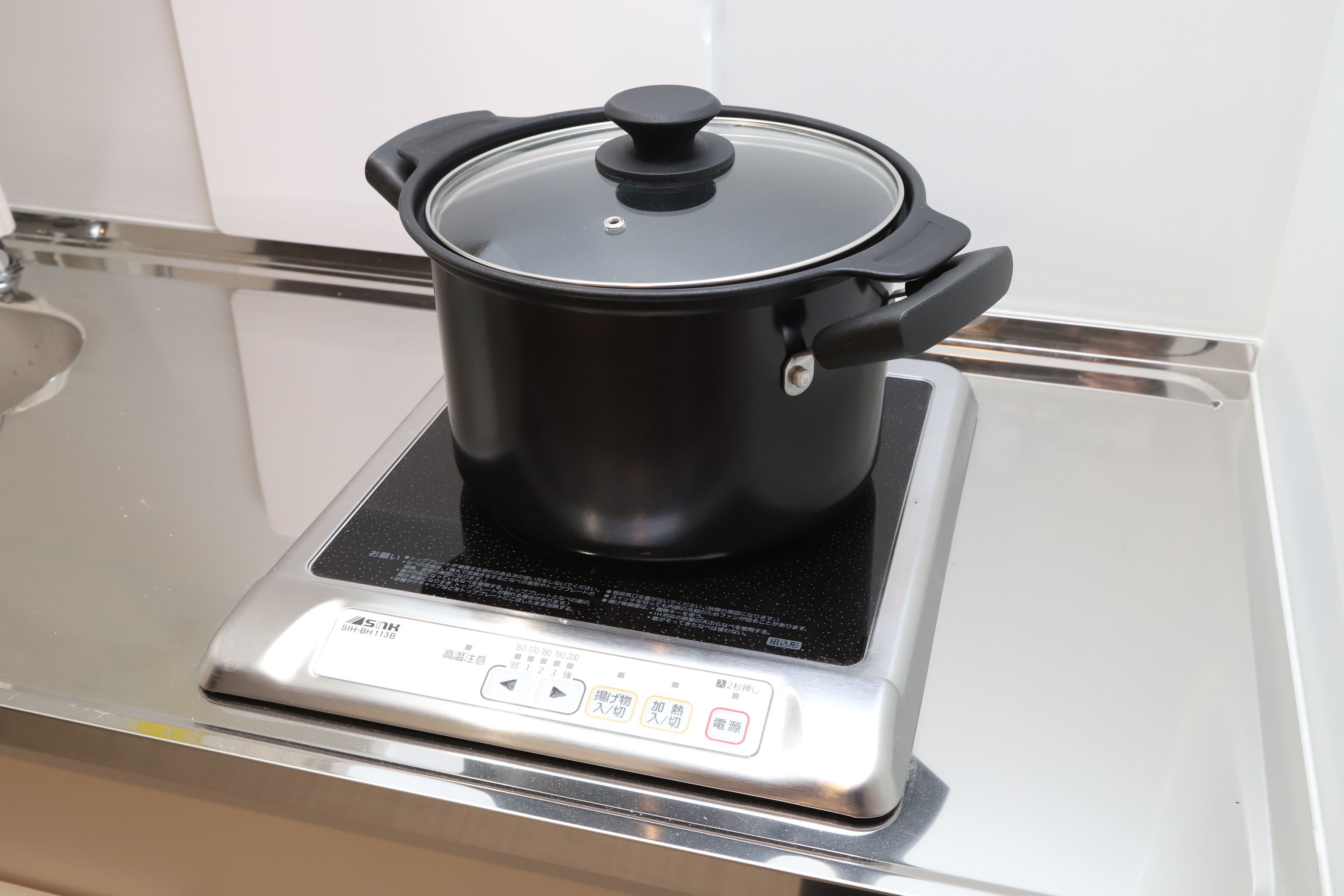 A black pot on a stainless steel induction cooktop with a digital control panel.