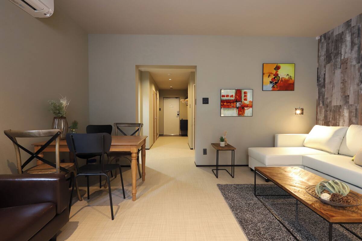 A modern living room with a white sofa, a wooden coffee table, and a dining area with a wooden table and chairs.