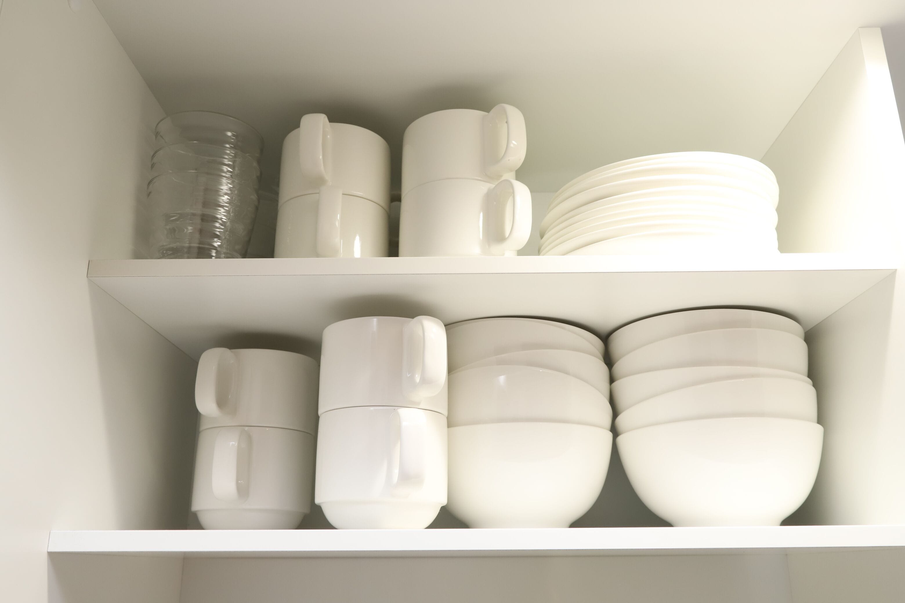 A white shelf with stacked white cups, plates, and bowls.