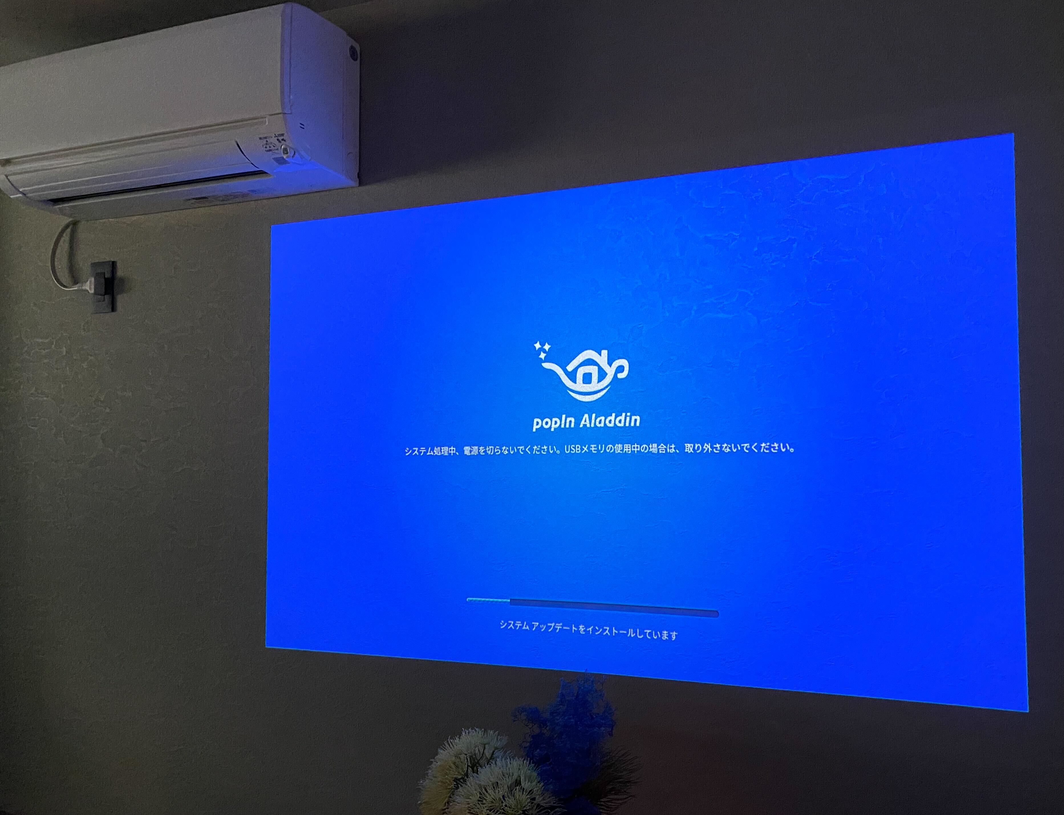 A room with a large screen displaying a software interface, an air conditioning unit, and a power outlet on the wall.