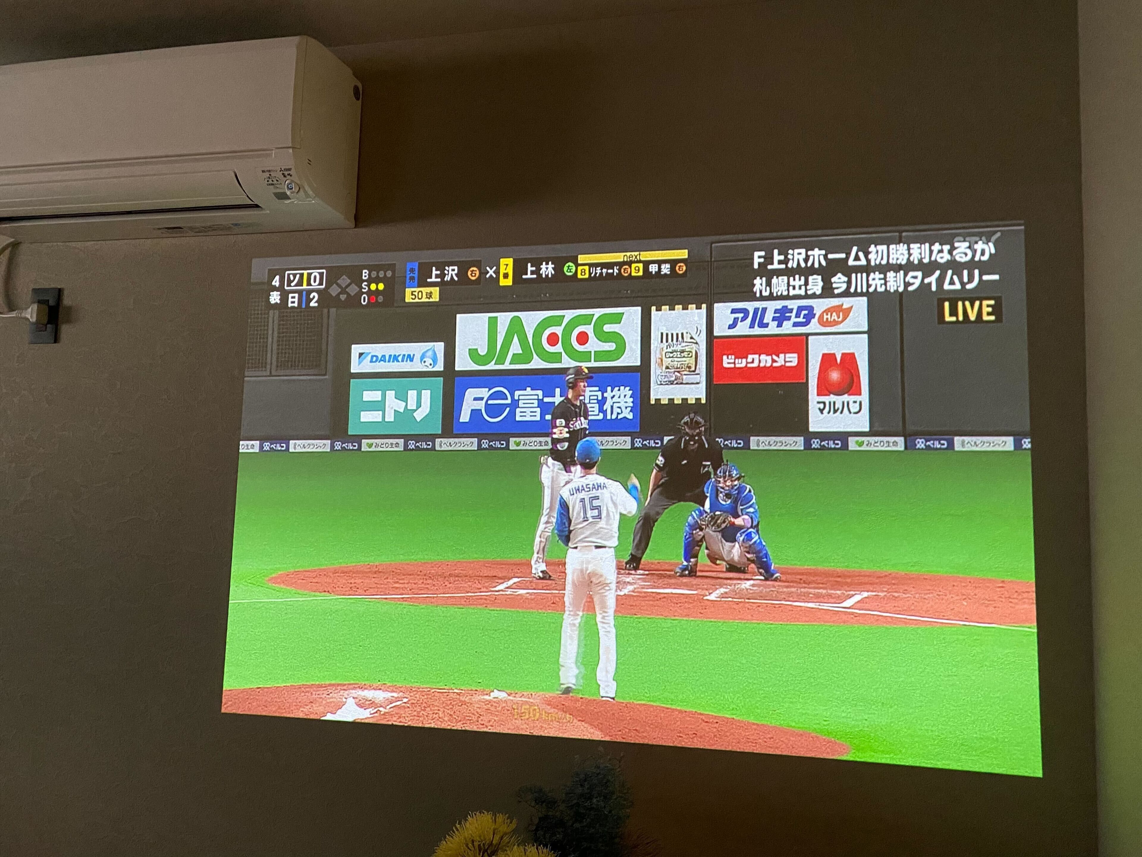 Un écran de télévision diffusant un match de baseball, montrant un joueur en train de frapper et un arbitre derrière lui.
