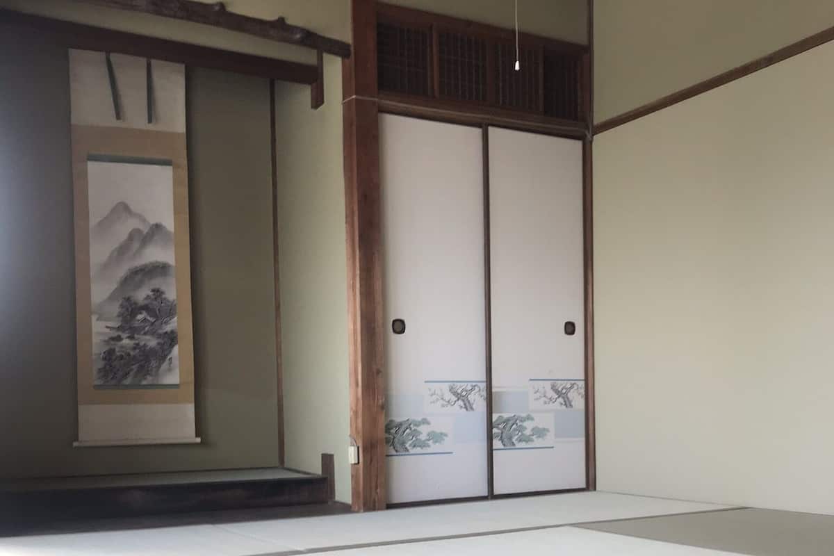 A tatami mat room with sliding doors and a traditional Japanese landscape painting.