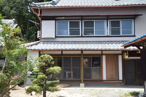 A traditional Japanese house with a tiled roof, large sliding doors, and a small garden with a tree and rocks. - Guesthouse Sangenya (Shirahama)