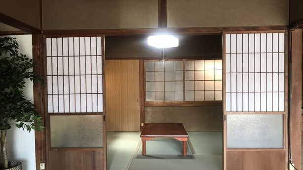 A traditional Japanese room with sliding doors, a tatami mat floor, a low wooden table, and a ceiling light. - Guesthouse Sangenya (Shirahama)