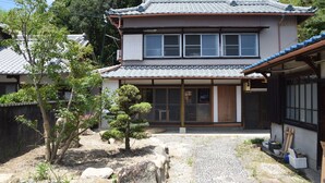 A traditional Japanese house with a tiled roof, a wooden front door, and a garden with rocks and plants. - Guesthouse Sangenya (Shirahama)