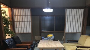 A traditional Japanese-style room with tatami flooring, a low wooden table, black leather chairs, and a yellow sofa. - Guesthouse Sangenya (Shirahama)
