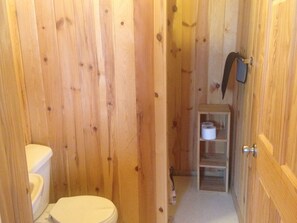 Ein Badezimmer mit Holzvertäfelung, einer Toilette und einem Ablagefach für Toilettenpapier.