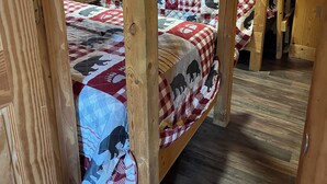Een slaapkamer met stapelbed, houten wanden en vloeren, met twee bedden voorzien van geruit beddengoed en een quilt met dierenprint.
