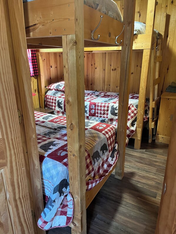 Une chambre avec des lits superposés, aux murs et au plancher en bois, comprenant deux lits avec une literie à carreaux et une courtepointe à motifs animaliers.