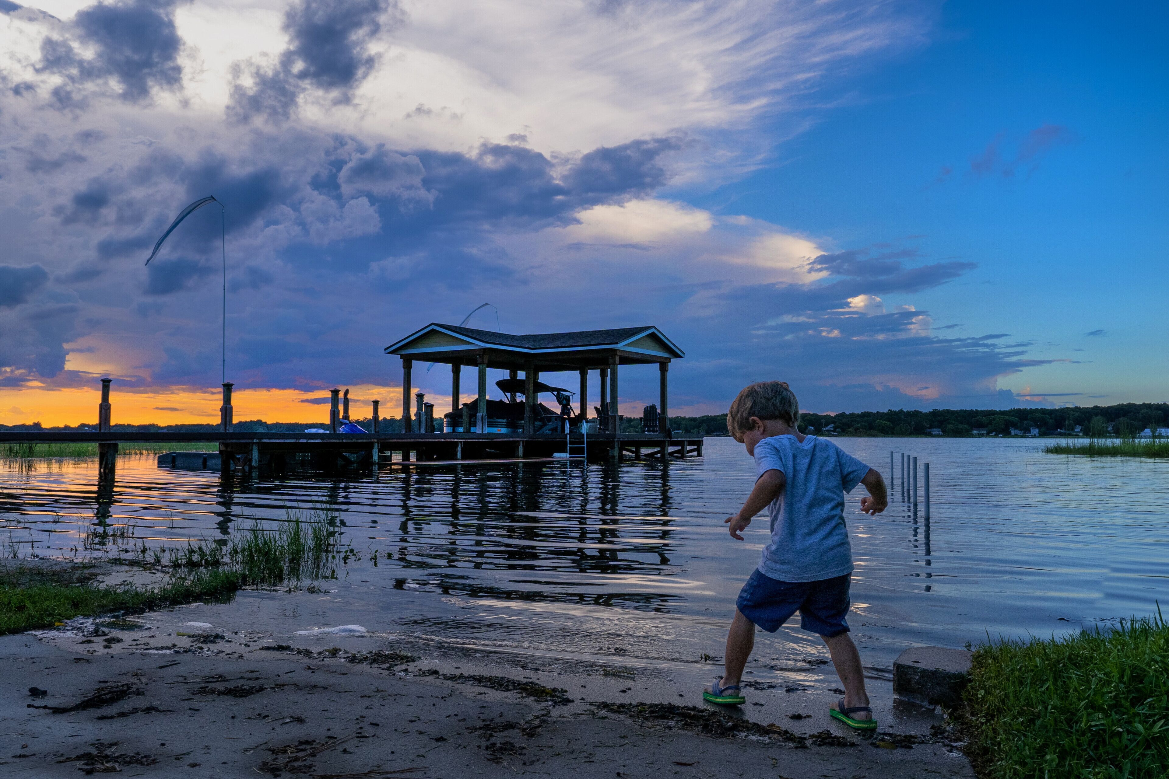 Ein Steg mit einem Gazebo, ein ruhiger See und ein Sonnenuntergang im Hintergrund.