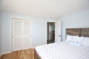Een slaapkamer met een houten hoofdbord, een bed met een beddekleed met dessin, en een witte deur met verstelbare lamellen.
