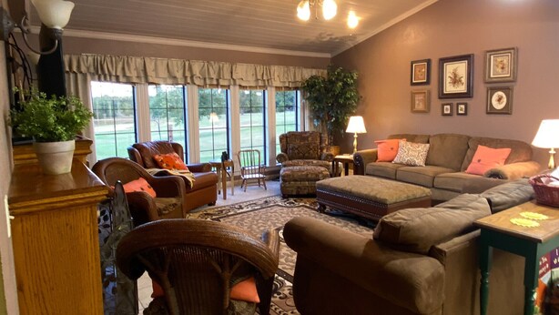 A cozy living room with a fireplace, comfortable seating, and large windows offering a view of the outdoors. - Located near the historic capitol of the Chickasaw Nation and Blue River (Tishomingo)