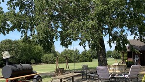 A picnic setup with a grill, benches, and chairs under a large tree. - Located near the historic capitol of the Chickasaw Nation and Blue River (Tishomingo)