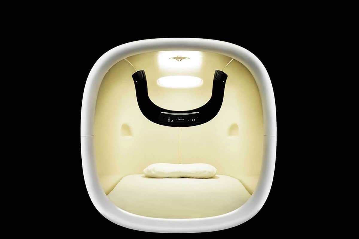 A modern, minimalist room with a curved white wall, a central light fixture, and a single white pillow on the floor.
